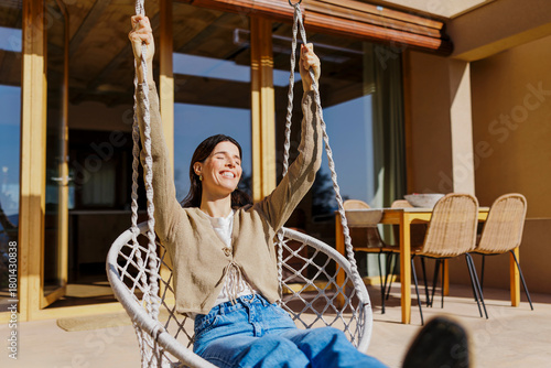 Young woman relaxing on a swing chair in a sunny, sustainable home patio.