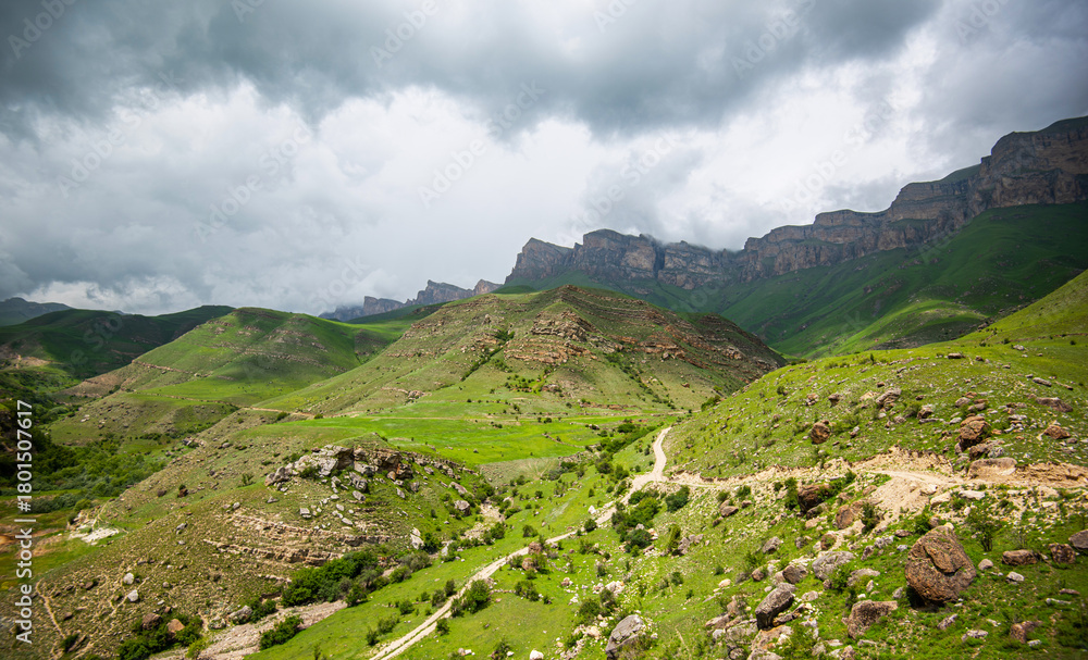 Fototapeta premium a majestic mountain range with distinct stratified rock formations and green slopes. Foreboding clouds loom overhead, a storm brewing, to the dramatic effect of the rugged landscape.