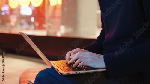 cinematic shot of A young man typing on a laptop at street at night, middle shot