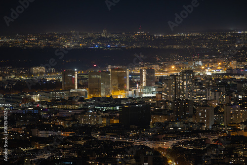 Aerial view of glimmering lights dance across the Parisian skyline, illuminating modern skyscrapers against the velvet night, Paris, Ile-de-France, France.
