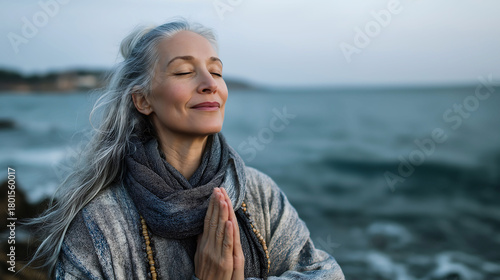Senior woman breathing fresh air with closed eyes, meditation on yoga pose while relaxing on calm beach with the sea view
