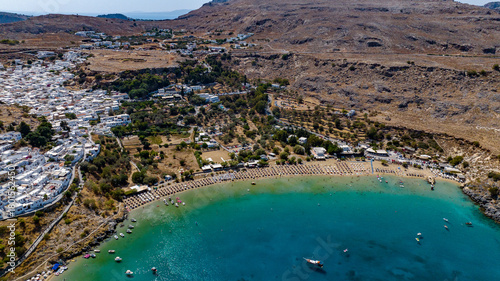 Aerial view of the turquoise bay embracing the golden beach below the whitewashed village and the ancient acropolis, Lindos, Rhodes, Greece.