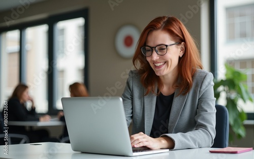Middle age European red and brown hair business woman using the laptop for work at workspace in the modern office, smiling on her face. High quality
