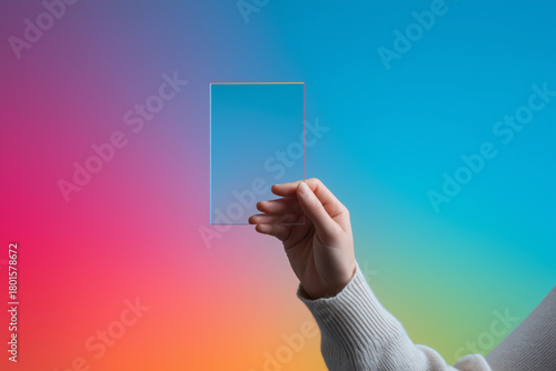 Female hand holding transparent rectangular glass pane against colorful background