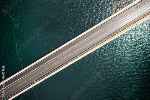 Aerial view of a straight bridge cutting through deep blue waters, a study in stark lines against fluid motion, Vallavik, Vestland, Norway.