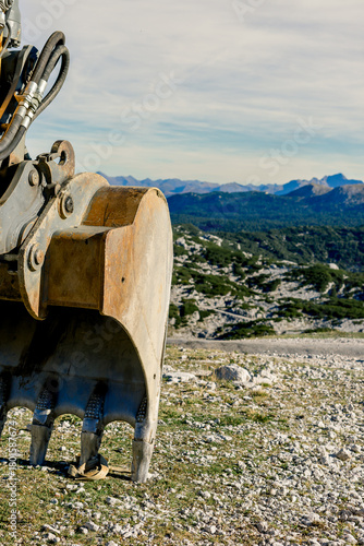 The bucket of a heavy excavator before the start of construction work on the top of a mountain against the backdrop of nature