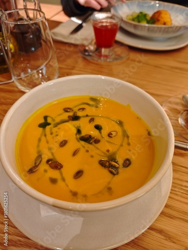 Creamy pumpkin soup with herds, sour cream, and balsamic drops served in a stylish bowl. 