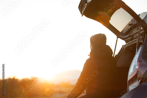 車のトランクを開け、朝日を眺める男性