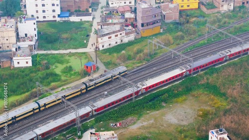 Aerial View of Indian Railway Tracks with Passing Trains Near Urban Residential Buildings and Greenery. Drone Shot of Passenger Train Passing Through Green Urban Corridor.