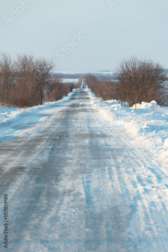 Scenic winter road covered in glistening snow leading through rural landscape, perfect for travel, adventure, or peaceful getaway concepts