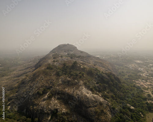 Aerial view of the rugged, rocky landscape of Mount Patti, its peak shrouded in mist, contrasting with the green trees dotting its slopes, Ado Awaye, Oyo, Nigeria..