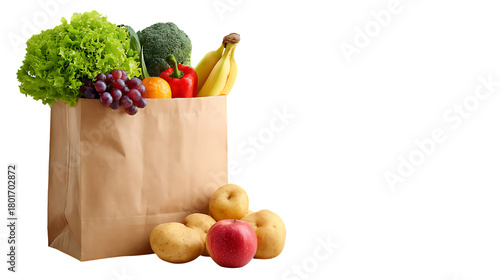 A paper grocery bag filled with fresh vegetables, lettuce, broccoli, bananas, grapes, red pepper, potatoes, and apples, placed with additional fruits and vegetables in front.