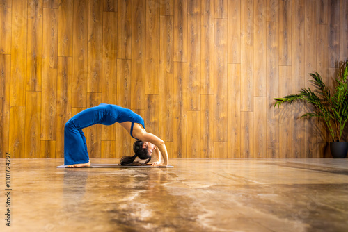 Yoga instructor performing wheel pose in studio with wooden wall