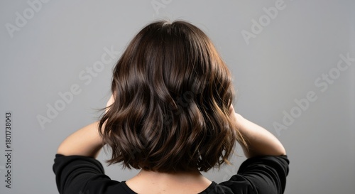 Back view of a woman with healthy shiny brown hair. Wavy brunette bob hairstyle after salon treatment. Hair care and beauty concept on a gray background with copy space