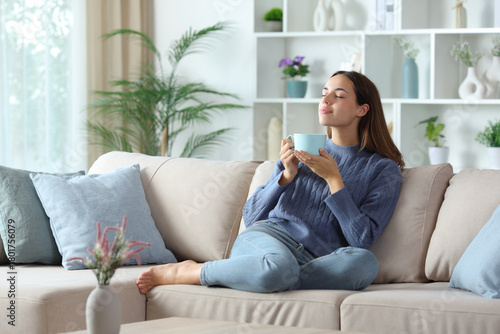 Relaxed woman in blue smelling coffee aroma at home