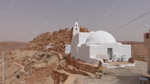Walking towards white mosque in Berber town of Chenini, built on spectacular mountain ridge in Tunisia
