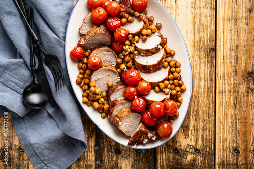 Roast pork tenderloin served with chickpeas and tomatoes in plate