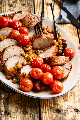 Roast pork tenderloin served with chickpeas and tomatoes in plate