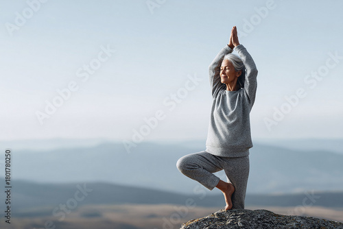 Serene older woman balances in tree pose atop a mountain. Illustrates healthy aging, mindfulness, and inner peace. Great for wellness, travel, or lifestyle.
