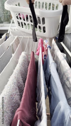 Vertical video social media - Closeup of a man’s hands adding a pair of black socks from a laundry basket to wet washing which is hanging on a clothes airer dryer, indoors.