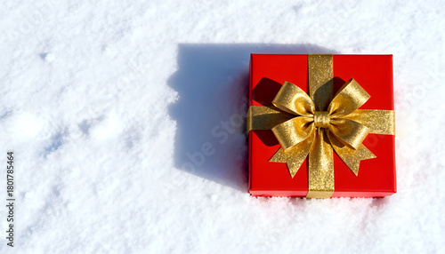 Red gift box with golden bow on white snow background. Simple holiday layout.