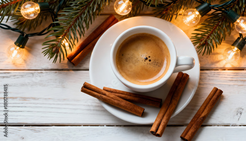 Cup of espresso surrounded by cinnamon sticks and Christmas lights. Festive coffee mood.