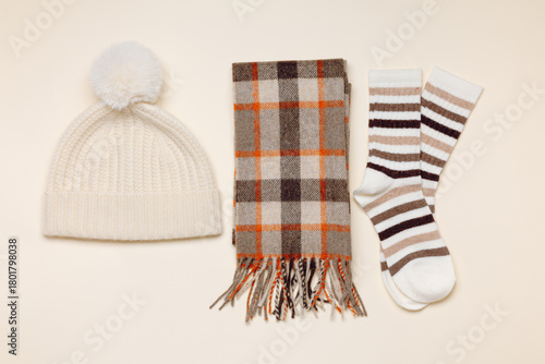 Cute knitted hat with checkered scarf and socks top view on beige background. Cozy winter and autumn fashion