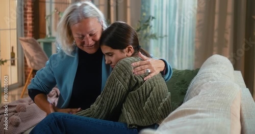 Grandmother warmly hugging her teenage granddaughter after a disagreement, smiling and sharing a heartfelt moment of reconciliation and family affection at home.