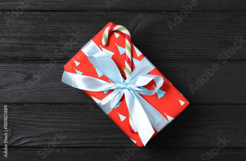 Decorated Christmas gift with candy cane on black wooden background, top view
