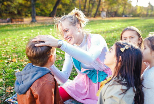 Female animator painting a child's face with a brush at an outdoor birthday party in a park.