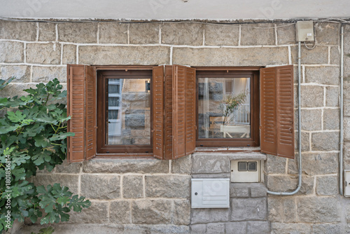 Front view of a village house with a gray granite facade in a coursed course and wooden balconies adorned with flowers, preserving the original character of the construction