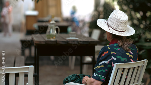 A close-up, cropped image featuring a person viewed from behind, wearing a classic woven straw sun hat with a brown band. The person is also wearing a dark shirt with a vibrant, repeating, abstract