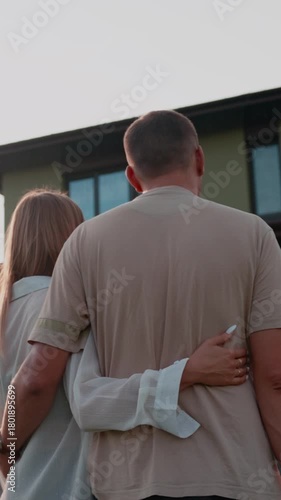 Young married couple hugging and looking at their dream home, celebrating their new life together and achieving their real estate goals while standing in the backyard during a warm sunset