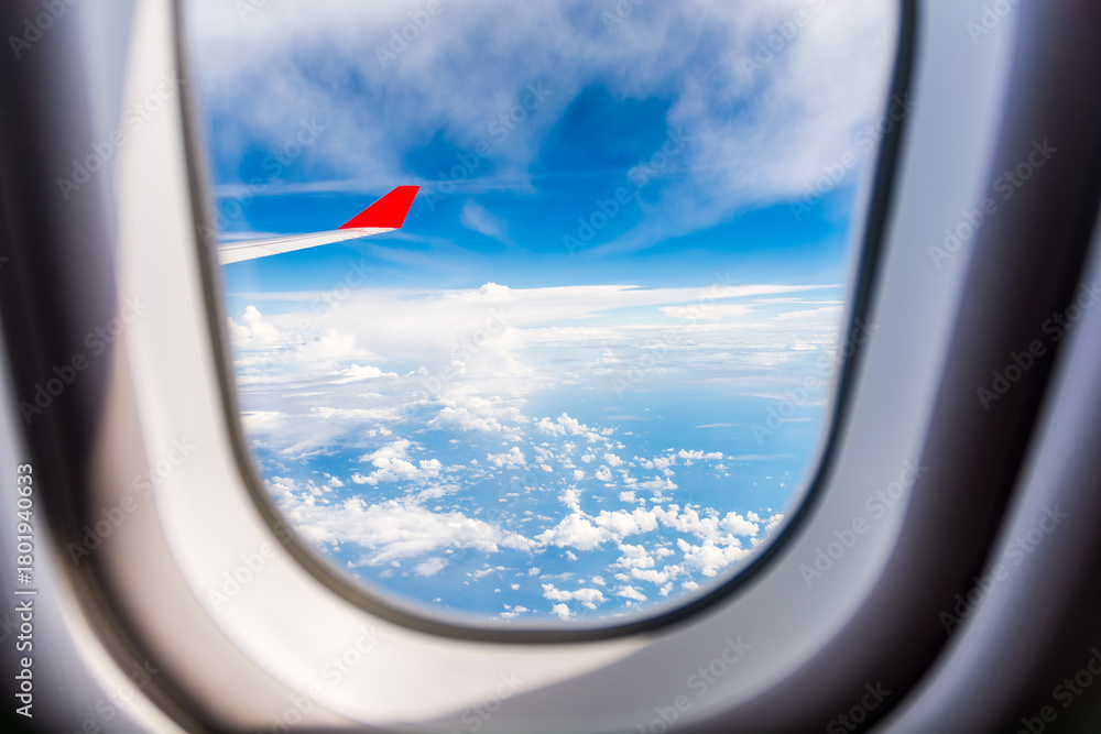Obraz premium Scenic view through an airplane window showing the white wing and red tip against a clear blue sky,