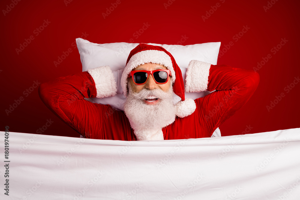 Obraz premium Cheerful Santa Claus lying in bed with sunglass smiling on a festive red background, spreading holiday cheer and joy