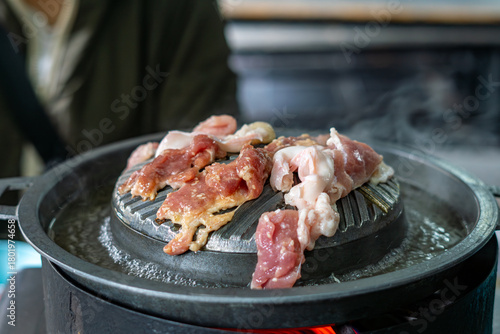 Close-up of Thai-style barbecue grill pan, known as Moo Kratha, with pork belly, shrimp, and vegetables cooking on a hot grill and soup. Popular Asian dining experience in Thailand.