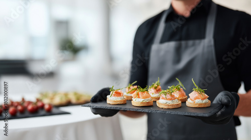 Catering professional serving elegantly prepared salmon canapes on a black slate tray, wearing uniform and gloves, providing luxury appetizer service at an exclusive event