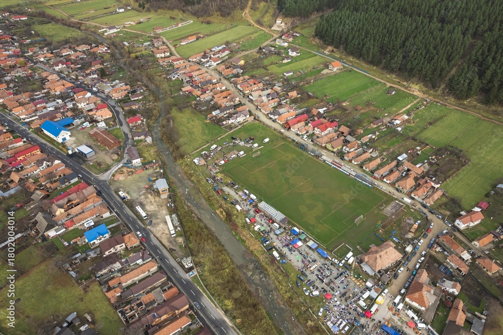 Naklejka premium From above, Zarnesti showcases its scenic beauty with a bustling football field surrounded by lush greenery. Colorful houses dot the landscape, reflecting rural life in Romania