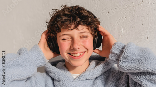 Boy in a blue fleece hoodie holds headphones and smiles — lively child portrait with audio emphasis.