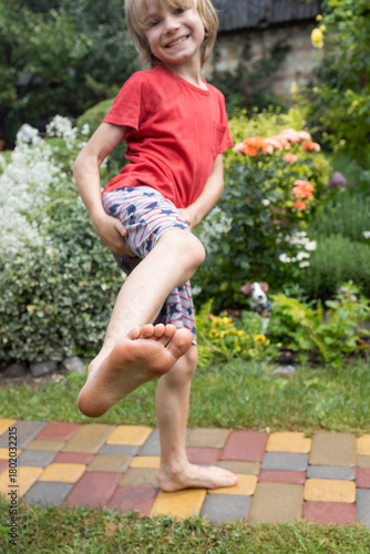 Walking barefoot on wet grass after the rain. A barefoot child stands on the sidewalk, showing one foot. A fun and exciting childhood. Playfulness, the energy of nature, childish freedom, a good mood