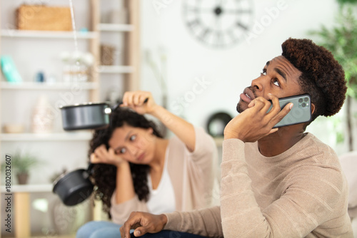 man calling while woman using utensil for collecting water leaking