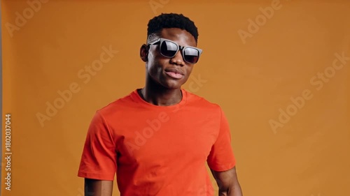 Dynamic Studio Shot of Young African American Man in Orange Clothing and Shades Against Orange Background