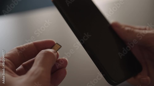 Detail cropped shot of unrecognizable man inserting nano sim card into new smartphone tray sitting on desk, illustrating mobile service transfer, setup, and device upgrade connectivity, slow motion.