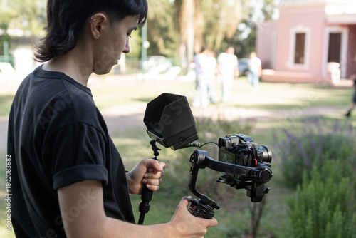 Primer plano de joven con cámara en mano y monitor digital filmando secuencia al aire libre