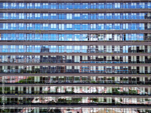 Bottom view of office building window close up, reflection and perspective. Modern architecture with sun ray. Glass facade on a bright sunny day with sunbeams on the blue sky.