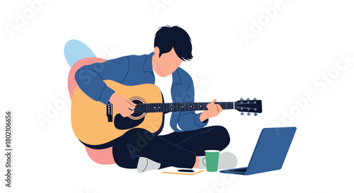 A young man sits cross-legged on a cushion, playing an acoustic guitar while looking at a laptop, with a mug nearby, suggesting a relaxed learning or creative session.