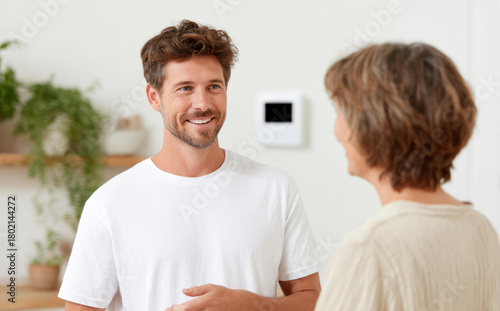 Friendly smiling air conditioner technician man explaining new thermostat to woman customer. repairman provides professional home service and consultation