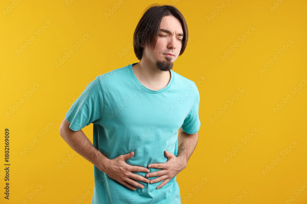 Obraz premium Man suffering from stomach ache and nausea on yellow background
