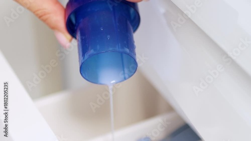 Hand pouring liquid laundry detergent or fabric softener into washing machine — clothes washing and home cleaning routine concept	