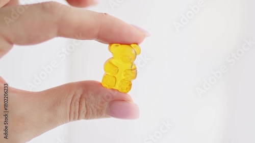 Close-up of fingers holding a soft gummy bear candy made of gelatin. Concept of CBD gummies, vitamin supplements for kids, healthy treats, and nutritional candy. Colorful chewy texture symbolizing fun